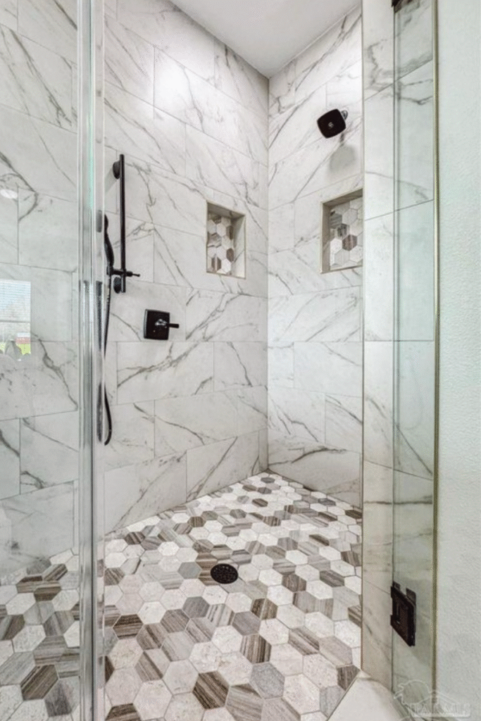 Modern walk-in shower with marble tile walls, built-in niches, and hexagon tile flooring.